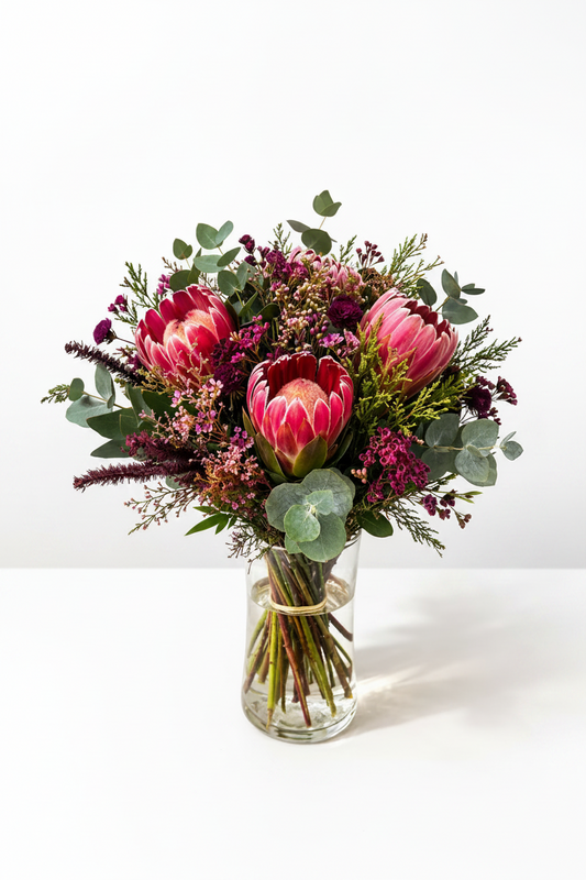 Elegant protea bloom arrangement in a clear glass vase, featuring vibrant, fresh flowers and lush greenery.